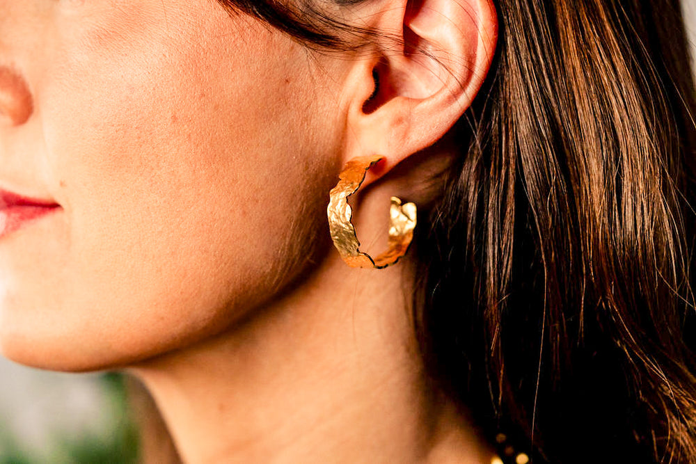 a model wearing a large hammered gold hoop earring.