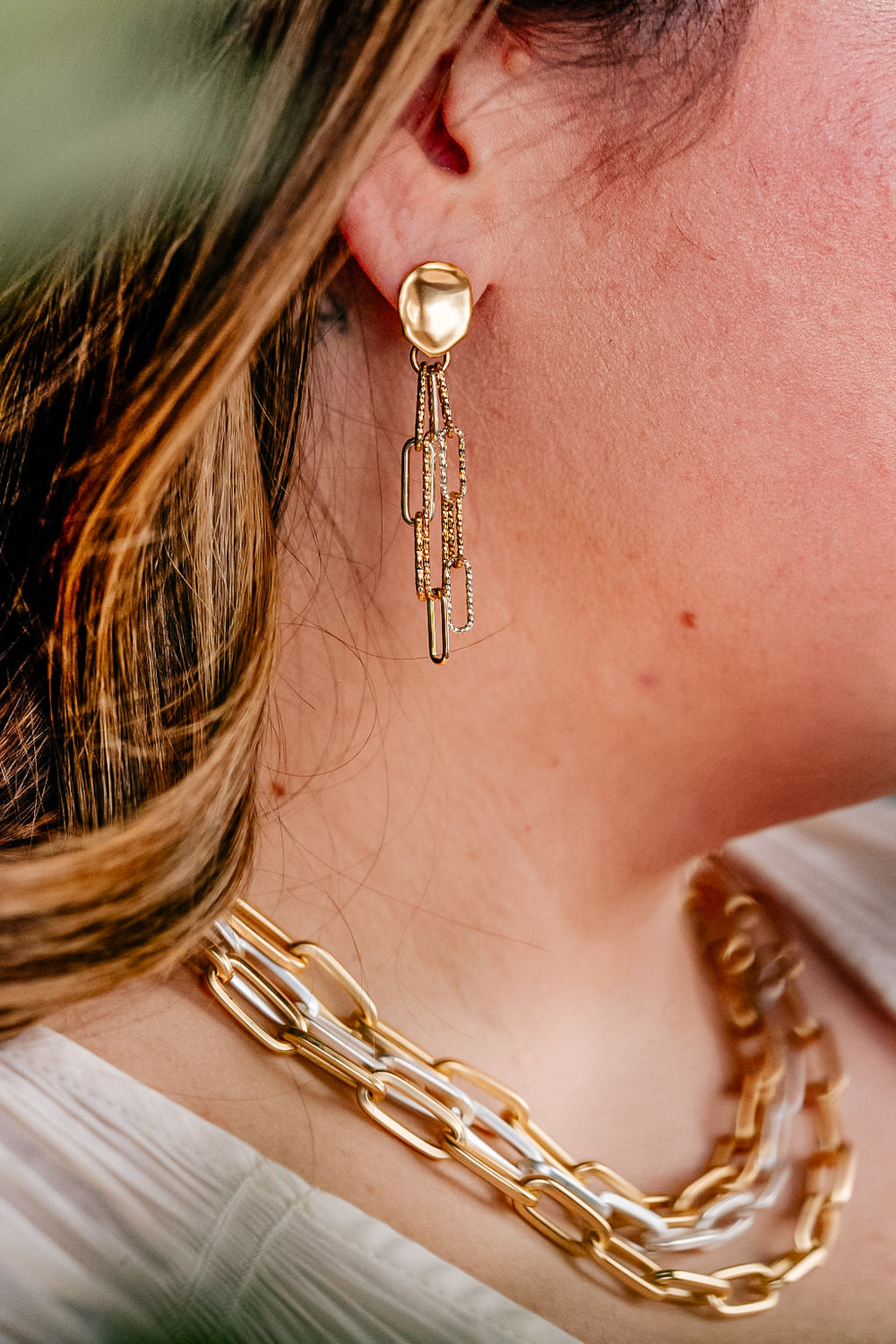 A model wearing a silver and gold paperclip chain earring